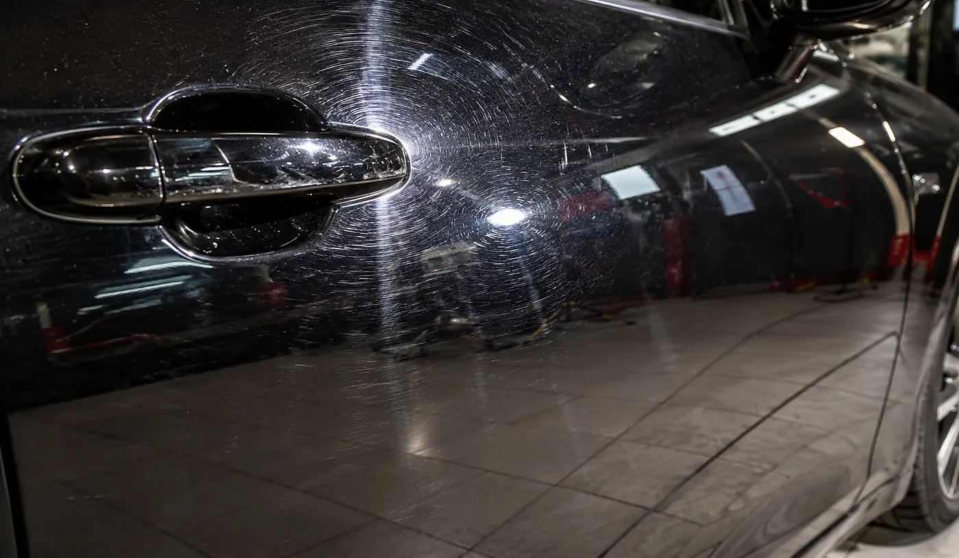 Schwarze Fahrzeugtür mit feinen Kratzern und Waschanlagen-Hologrammen vor der Politur